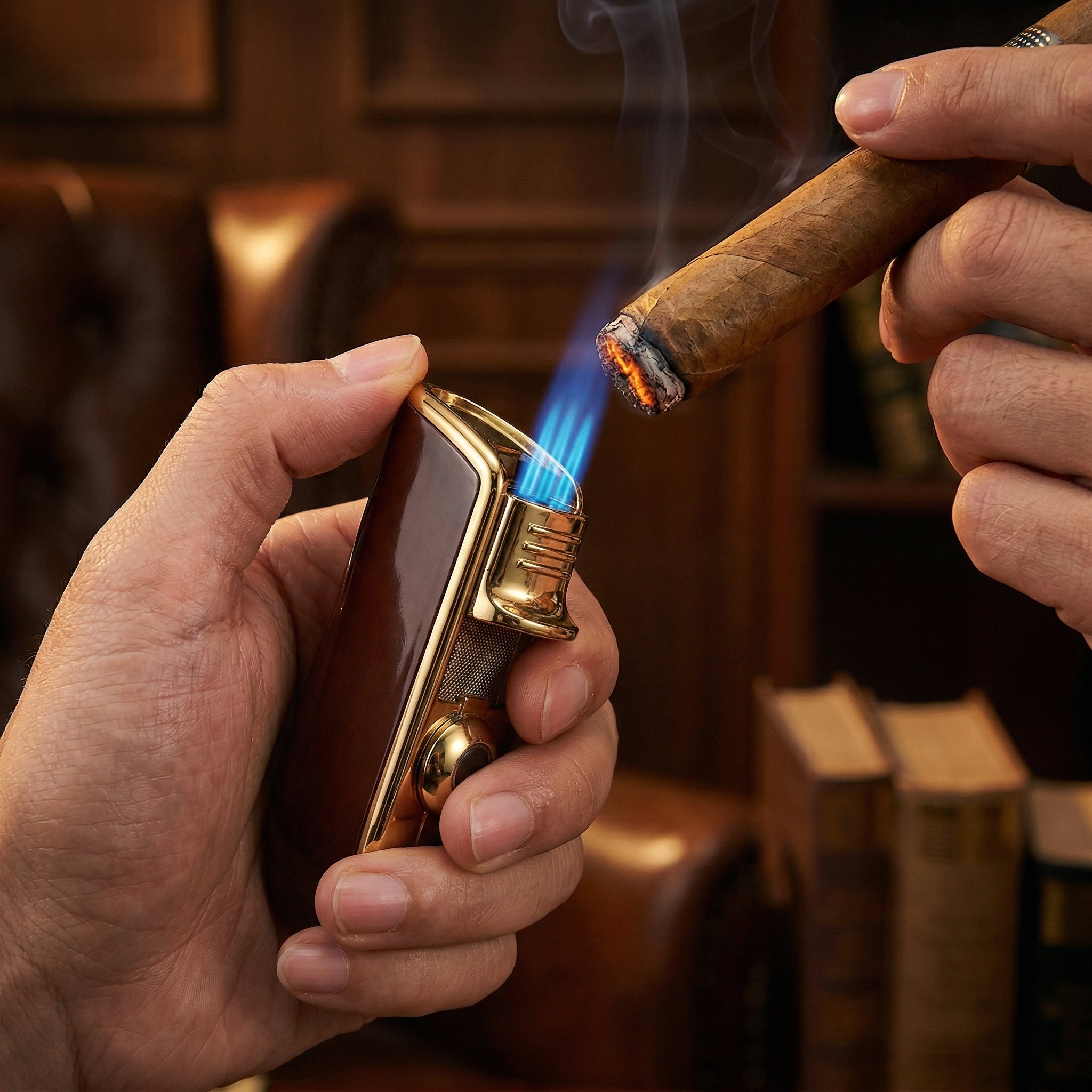 Lifestyle action shot of hands lighting a cigar using a wood-grain and gold triple-jet torch lighter. Three intense blue flames ignite the cigar tip, creating glowing embers and rising smoke within a warm, sophisticated lounge setting.